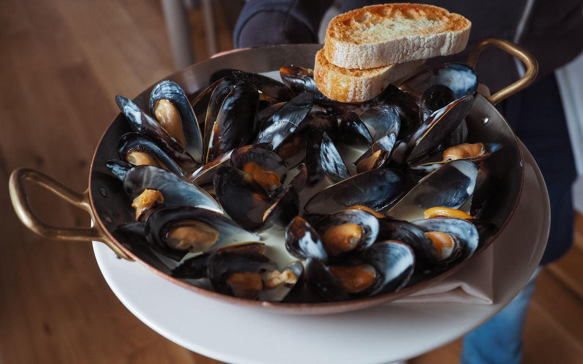 A pan of steamed mussels in a creamy broth served with toasted bread