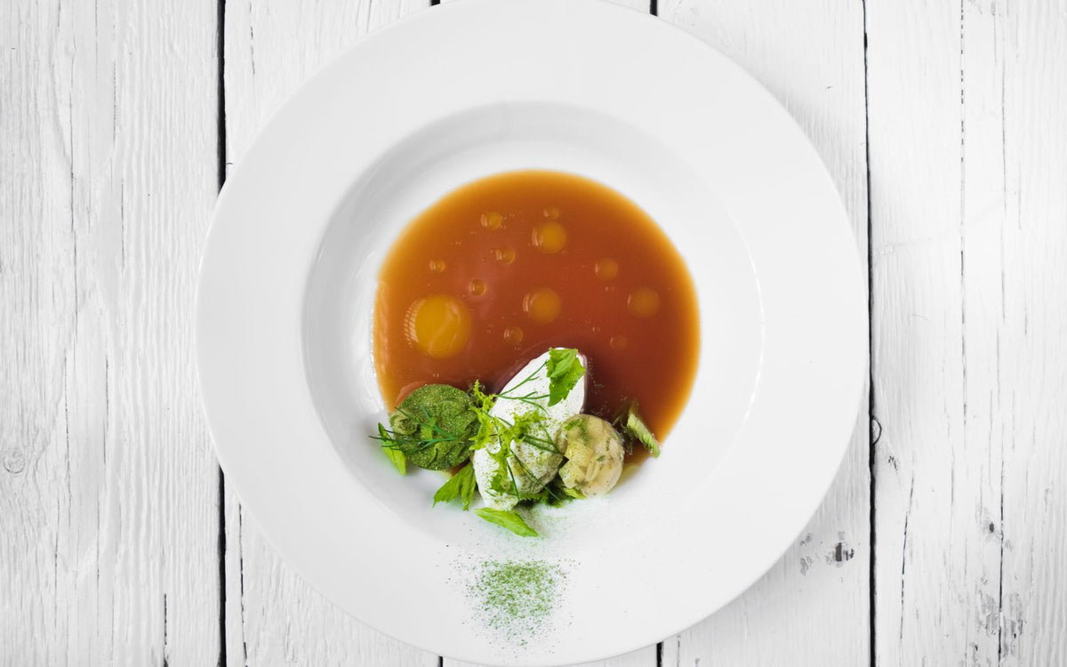 A shallow bowl of clear amber dashi broth with a herb garnish