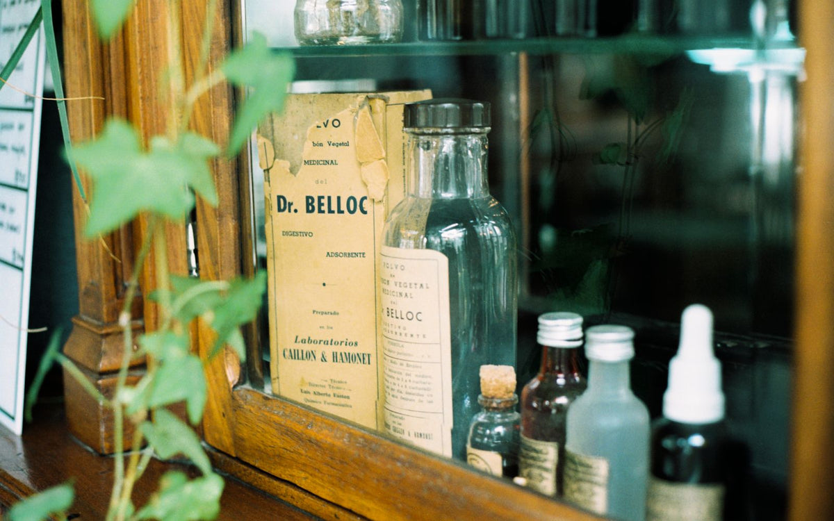 A collection of vintage apothecary glass bottles in a wooden cabinet