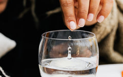 Close-up of a fingertip dropping a single drop of water into a glass