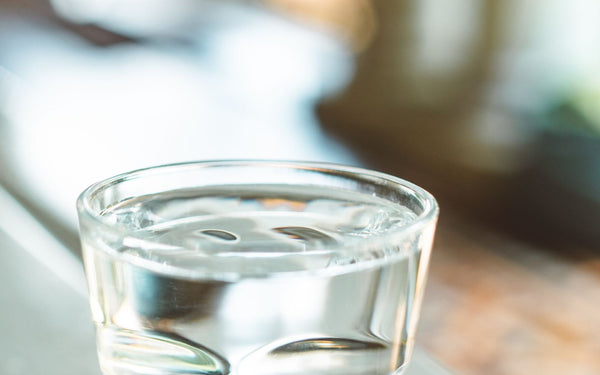 A clear glass of water on a sunlit window sill with a soft bokeh background