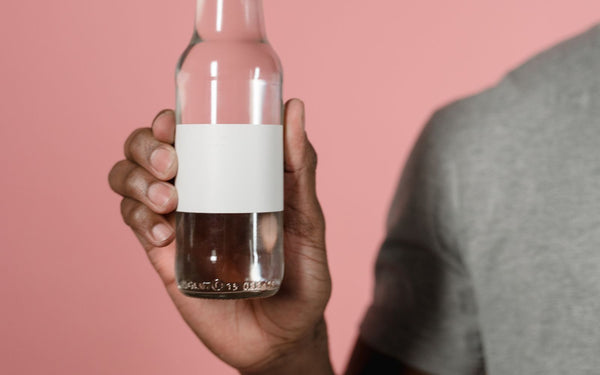 Close-up of a hand holding a glass supplement bottle with a blank label