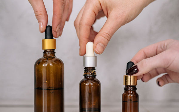 Hands holding three different sized amber dropper bottles side by side