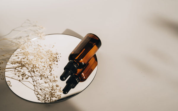 Minimalist still life of an amber glass dropper bottle on a mirrored surface