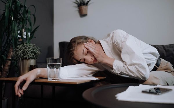 A tired woman in business attire resting with her head on a table, showing signs of fatigue